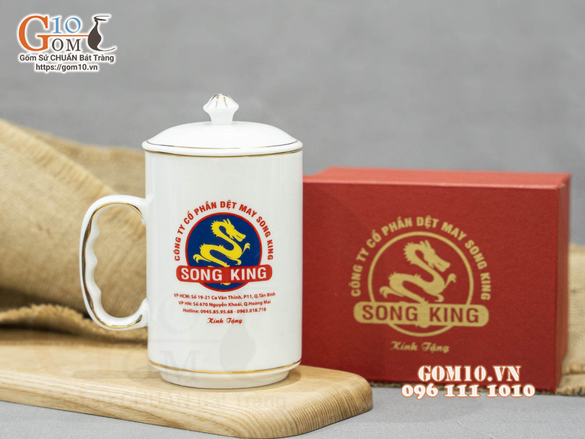 Cốc sứ dáng cao quai nắm men trắng có nắp kẻ chỉ vàng in logo Công ty Song King, 500ml