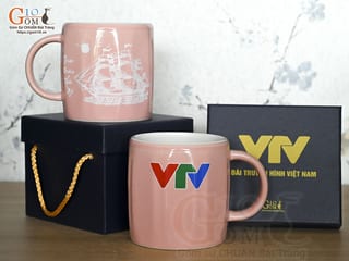 Cốc sứ dáng lục giác quai tròn màu hồng cảnh Thuận Buồm Xuôi Gió, in logo VTV